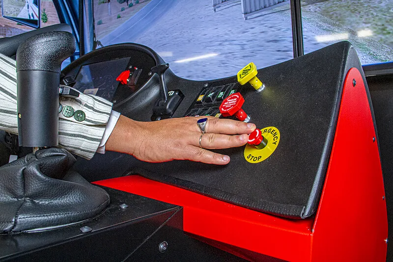 Mano accionando los mandos de una consola de simulador junto a la palanca de cambios y la parada de emergencia