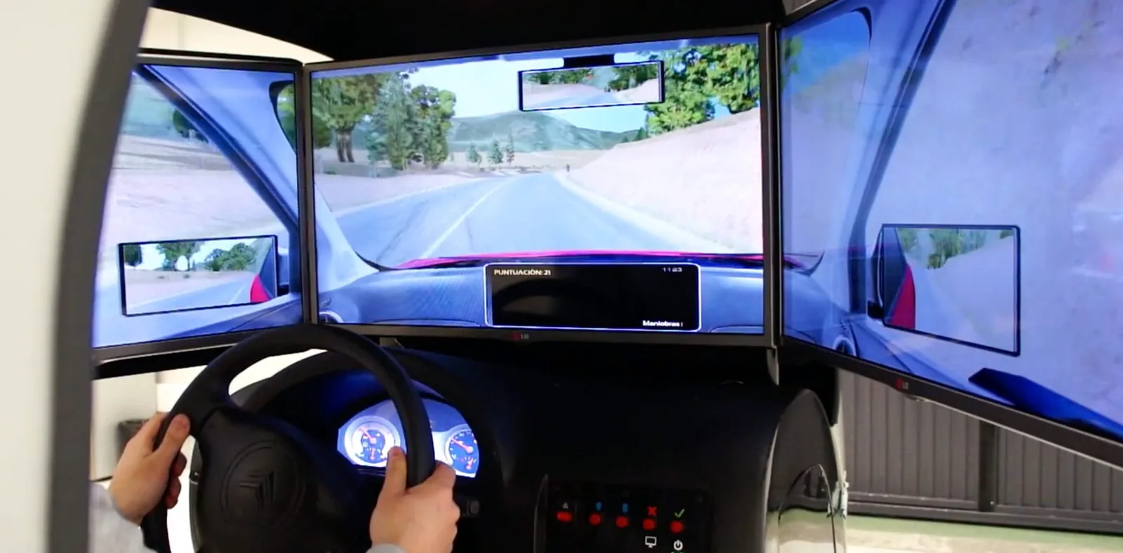 Manos al volante de un simulador de conducción frente a tres pantallas envolventes con una carretera