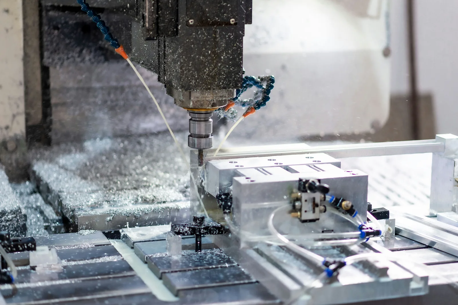 Centro de mecanizado CNC fresando piezas de aluminio sujetas en la mesa, con refrigerante y virutas